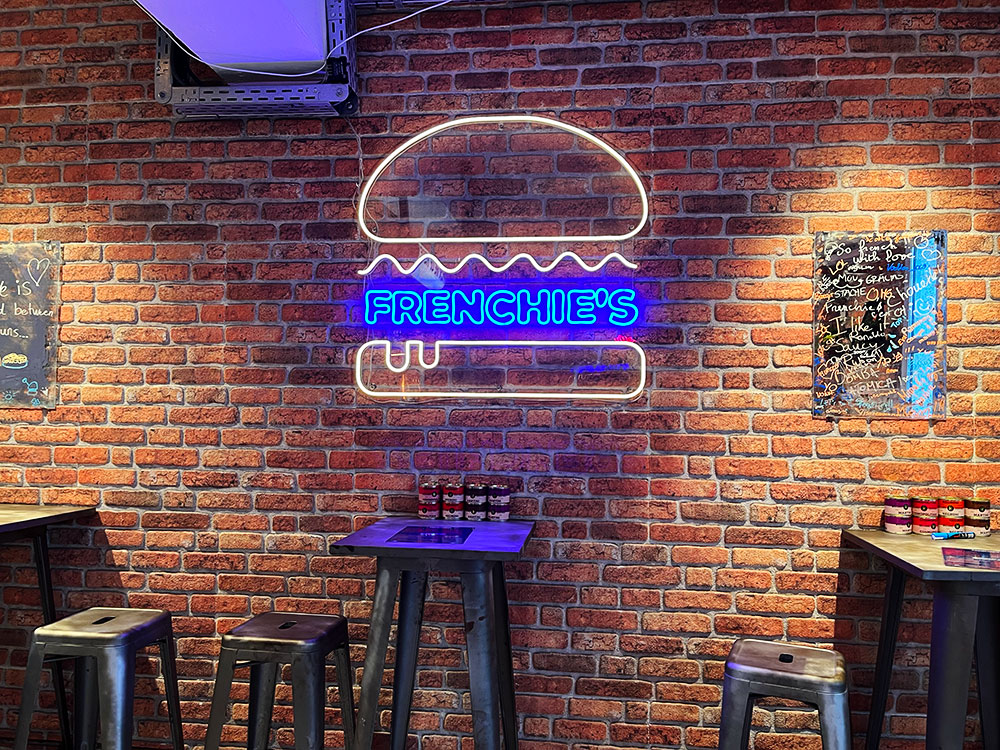 Frenchie's neon burger and name sign on a brick wall