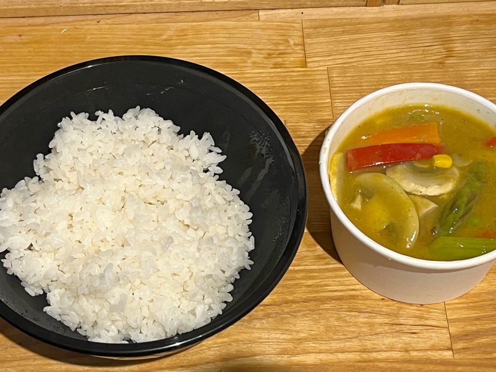 A bowl of white rice next to a small cup with green curry and vegetables